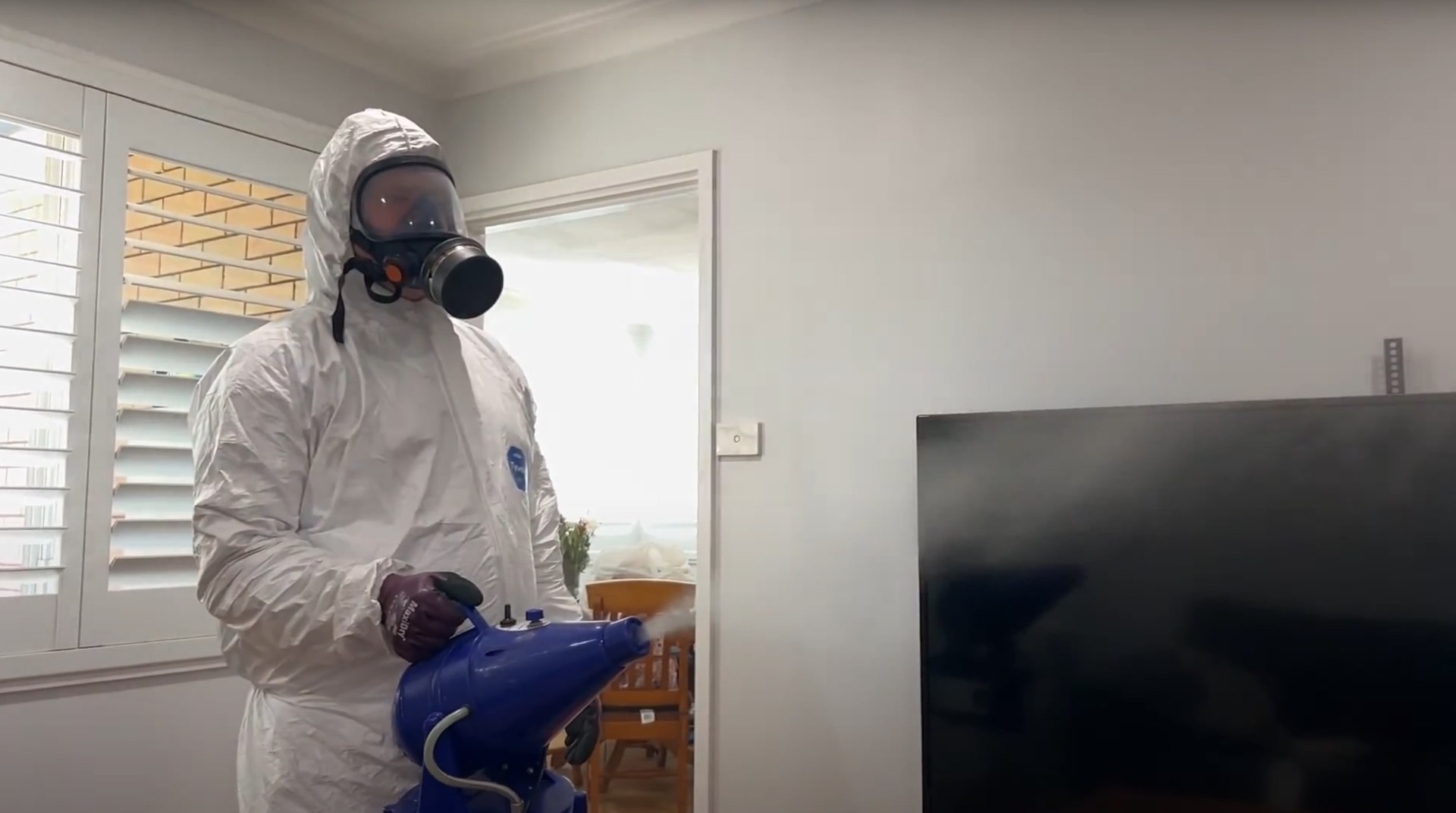 Professional water damage restoration technician in protective suit using specialized equipment